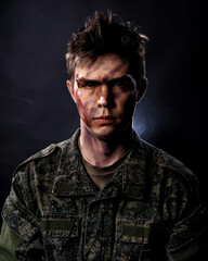 Portrait of a young soldier in uniform and combat coloring with bruises and scars on a black...