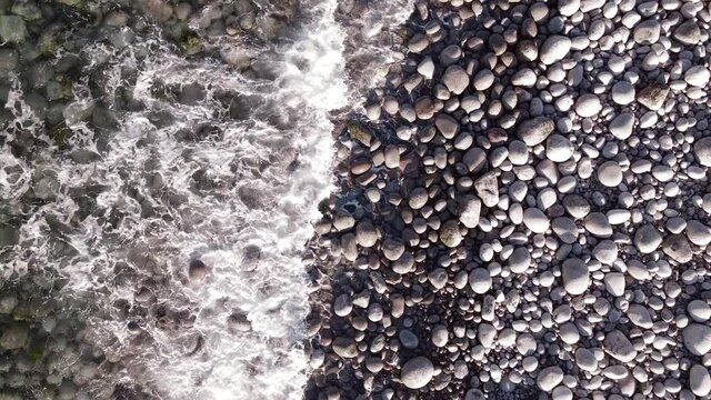 winter aerial flight top over waves rolling on artic ocean shore with round stones, ocean waves at storm