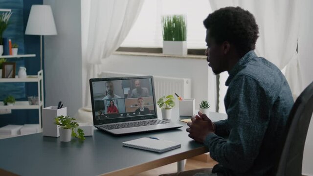 Black man remote worker working from home taking online office call with partners and colleagues, greeting them. Computer user from home office on video internet conference via webcam conference call