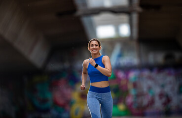 Young woman jogging in urban setting with graffiti in background