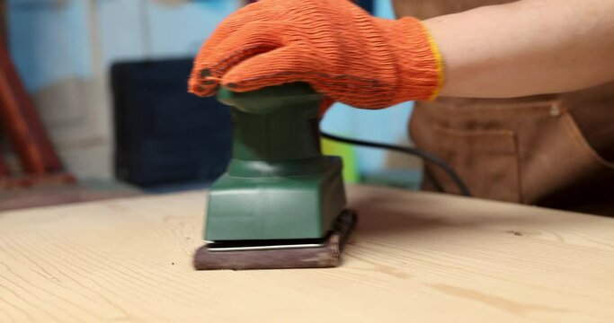 Closeup of carpenter sanding wooden planks with electrical sanding machine. A carpenter grinds wood with sander machine