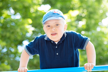 Happy boy with Down syndrome in the park against a background of green grass, close-up portrait of...