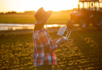 Farmer standing in field using controller for driving tractor at sunset