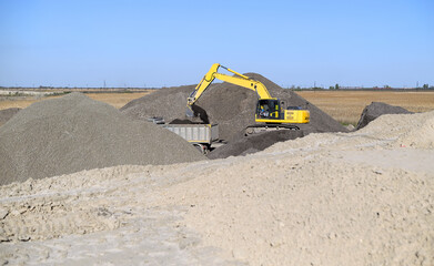 yellow excavator involved in the construction of a highway loading rubble into a truck