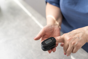 Middle-aged grey-haired woman feels unwell, measuring blood pressure and pulse pulse rate. Senior female using oximeter at home