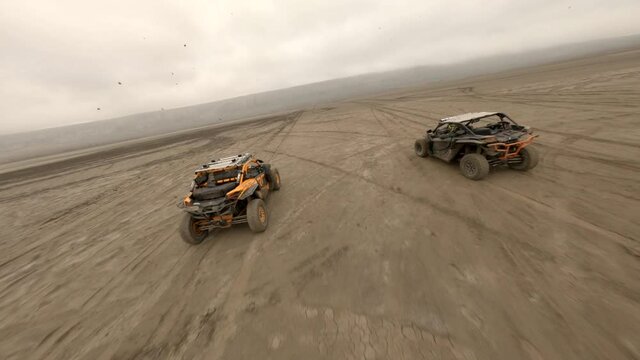 Aerial shot riding competition buggy rally cars driving at sand dessert with dust smog. Shooting from sports fpv drone active male running fast movement over countryside valley with mountain top view