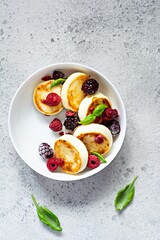 Fresh cottage cheese or ricotta  pancakes (syrniki,fritters) on a white plate with fresh berries on a blue background. Delicious healthy breakfast.  Ukrainian, Russian cuisine sweet food.