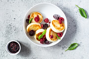 Fresh cottage cheese or ricotta  pancakes (syrniki,fritters) on a white plate with fresh berries on a blue background. Delicious healthy breakfast.  Ukrainian, Russian cuisine sweet food.