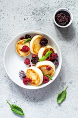 Fresh cottage cheese or ricotta  pancakes (syrniki,fritters) on a white plate with fresh berries on a blue background. Delicious healthy breakfast.  Ukrainian, Russian cuisine sweet food.