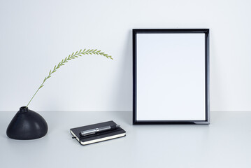 Empty black picture frame mockup. Irregular shaped black ceramic vase with blade of grass. Black...