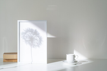 Empty white picture frame mockup in sunlight. Long shadow effect of shower head in the frame. Books...