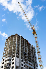 Fototapeta premium Construction of a multi storey high house. Crane at construction site against blue sky with clouds