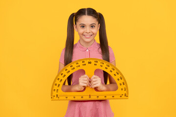 happy child hold school math tool protractor ruler on yellow background, school