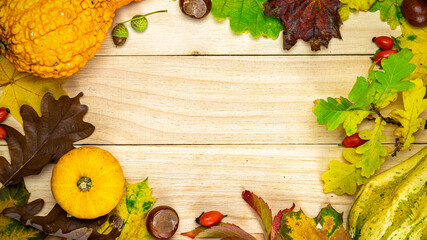 Flat lay autumn. Natural harvest with orange pumpkin, fall dried leaves, red berries and acorns, chestnuts on wooden background in shape frame. For seasonal offers and holiday post card, top view.