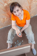 DIY assembly of furniture flat pack at home. Mature European woman holding fasteners in palm of her hand.
