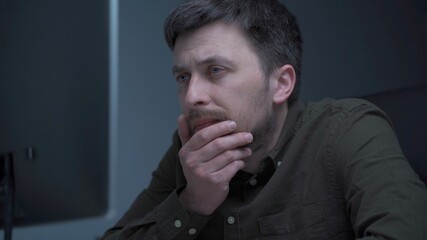 Tired male working on computer. Sad exhausted man at home office. Stressful work, stress at workplace. Software developer looks very tired during completion overtime of project, working on computer