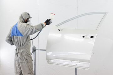 Man in overalls paints the car door using factory technology. Man in a mask, respirator. spray...