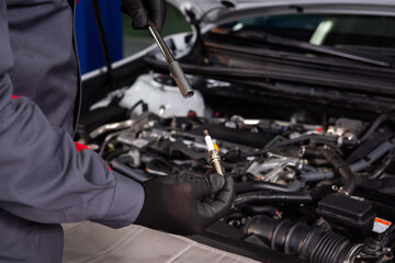 Obraz premium mechanic makes diagnostics of the car in the engine. car service and audit by an employee in a large car service. candle replacement. black mittens and car tool