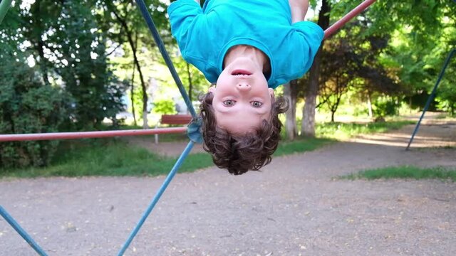 Curly boy climbing monkey bar outside at playground. Child plays climbs metal bar at park