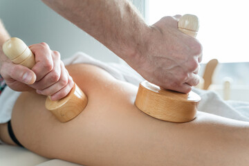 Close up on back of unknown woman having madero therapy massage anti-cellulite treatment by professional therapist holding wooden tools in hands in studio or salon with copy space