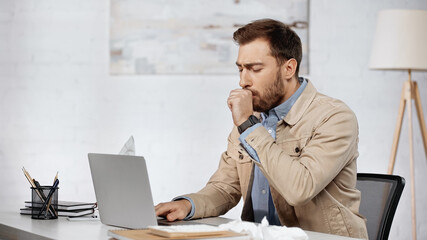 allergic businessman couching near laptop on desk