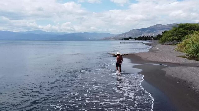 palmar de ocoa, republcia dominicana, junio 3 2021 - Hombre mayor caminando descalzo en la bah&iacute;a de la playa de palmar de ocoa, vista de drone amplio.