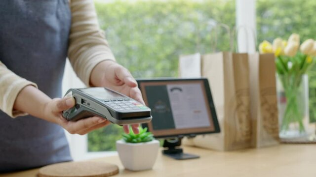 Close-up hand asia woman people work in small sme coffee cafe shop store owner use cashless wifi qr code nfc scan app smart pos reader sale in take out food drink order in urban city life contactless.