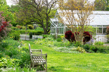 Landscape view of glass greenhouse in a park with bushes, trees, growing plants and flowers.