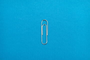 silver paper clip on blue background. realistic paperclip for binding paper and notes. silver metal...