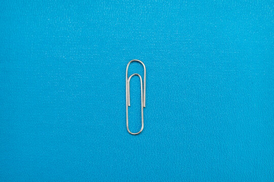 silver paper clip on blue background. realistic paperclip for binding paper and notes. silver metal fastener for office stationery.