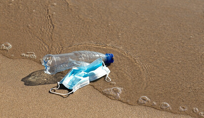 Fototapeta na wymiar A plastic bottle lies and medical mask on the beach and pollutes the sea . The concept of pollution control of the seas and oceans by plastic.