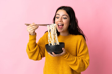 Young caucasian woman isolated on pink background holding a bowl of noodles with chopsticks and...