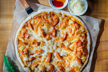 Homemade pizza on brown paper on wooden table with green leaf and white cream