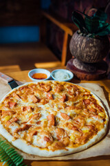 Homemade pizza on brown paper on wooden table with green leaf and white cream