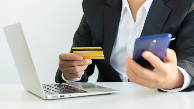 A young woman pays with a credit card online while making an online purchase on a laptop. Successful business people transact using mobile banking application.