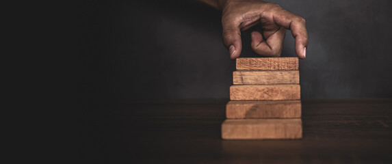 Close-up hand is placing wood block tower stacked in stair step with caution to prevent collapse or...
