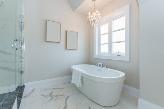Bright Clean Luxurious Bathroom with Chandelier and Window over a Stand Alone Bathtub