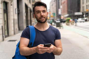 Young caucasian man on city street walking texting on cellphone