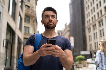 Young caucasian man on city street walking texting on cellphone