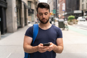 Young caucasian man on city street walking texting on cellphone