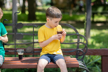 a 7-year-old boy in a yellow T-shirt drinks a cool brown drink from a glass to quench his thirst....