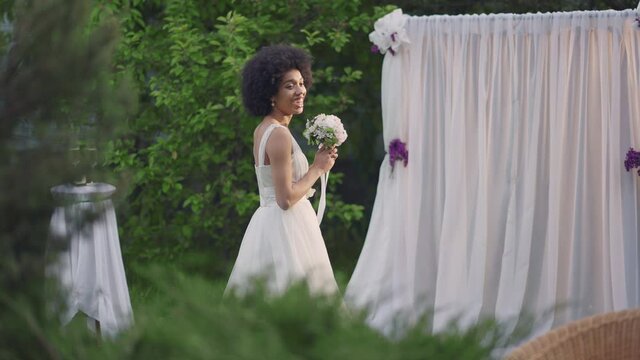 Side view portrait of smiling happy young African American bride in beautiful wedding dress looking back at guests preparing to throwing bridal bouquet. Cheerful slim woman on marriage ceremony