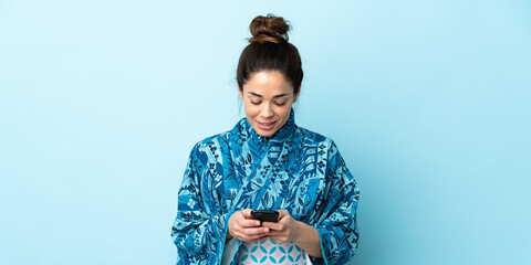Woman wearing kimono over isolated background sending a message with the mobile © luismolinero