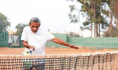 Elderly man practicing tennis near net - Concept of healthy and fit active old people.