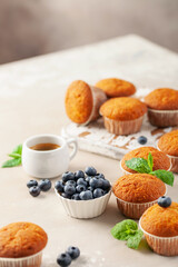 Muffins or capcakes with blueberries and mint, a cup of coffee on a wooden background.