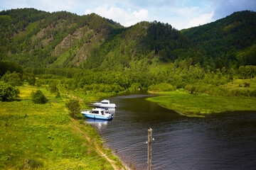 The yachts are located on the shore of a river or lake in a picturesque location. Around the forest, mountains. Unity with nature. Summer lake cruise.
