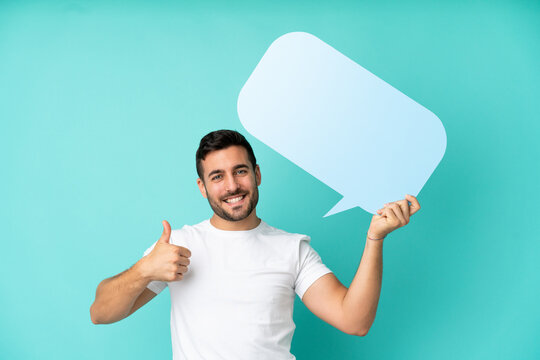 Young handsome caucasian man isolated on blue background holding an empty speech bubble with thumb up