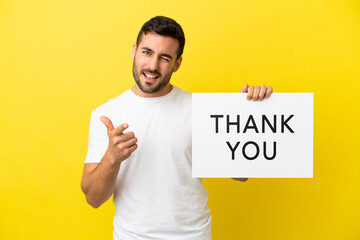 Young handsome caucasian man isolated on yellow background holding a placard with text THANK YOU and pointing to the front - obrazy, fototapety, plakaty