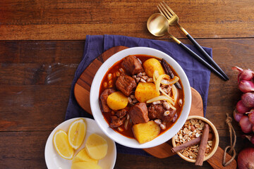 Thai food with rice Pork massaman curry with potatoes, peanuts, coconut milk and onions in a cup on a wooden table
