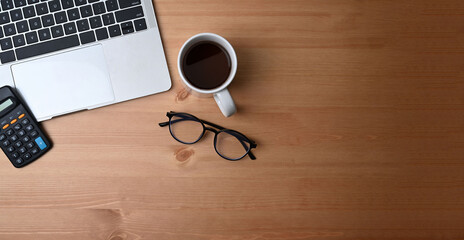 Accountant workplace with calculator, notebook, glasses, coffee cup, laptop and pen on wooden background.